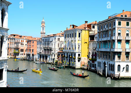 Gondoles voyageant le long du Grand Canal à Venise Italie avec rouge et blanc à rayures Bollards étés sur une journée avec un ciel sans nuages bleu brillant Banque D'Images