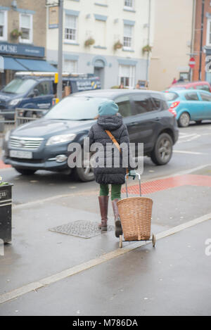 Météo : Bridport, England, UK vendredi 9 mars 2018 une femme avec un chapeau bleu et un panier en osier se dirige vers une voiture sous la pluie sur Tacloban High Street. Les ternes et les conditions humides doivent se poursuivre pendant le week-end avec l'amélioration attendue le lundi. Credit : PQ Images/Alamy Live News Banque D'Images