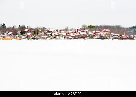 Brandaholm (Karlskrona, Suède) village d'attribution avec de petites cabines rouge en hiver paysage. Mer gelée recouverte de neige à l'avant-plan. Banque D'Images