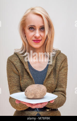 Les gens avec des fruits et légumes. Mode de vie sain. Young smiling woman showing pomme de terre sur la plaque blanche. Banque D'Images