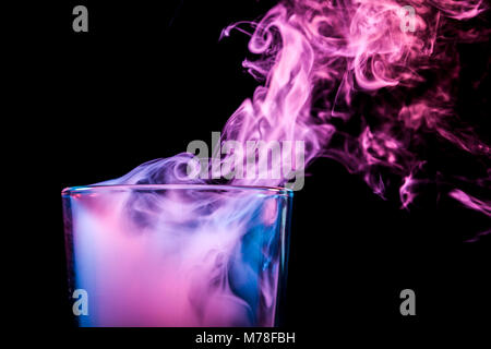 Un close-up de verre transparent en verre rempli d'une perruque d'un bleu, bleu, violet essuyer fume et se tient sur un fond noir isolé. Bongs en verre pour Banque D'Images