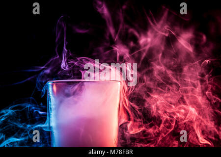 Un close-up de verre transparent en verre rempli d'une perruque d'un bleu, bleu, violet essuyer fume et se tient sur un fond noir isolé. Bongs en verre pour Banque D'Images