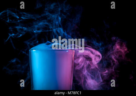 Un close-up de verre transparent en verre rempli d'une perruque d'un bleu, bleu, violet essuyer fume et se tient sur un fond noir isolé. Bongs en verre pour Banque D'Images