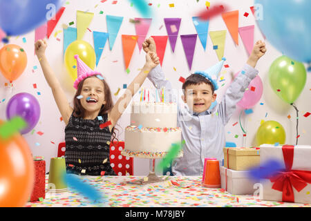 Heureux les enfants avec chapeaux de fête et un gâteau célébrant un anniversaire Banque D'Images