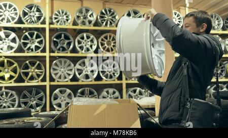 L'homme achète alloy wheels dans son atelier pour sa voiture. Il prend un disque de sa boîte et l'examine. La molette blanche est très belle et raide. Drawin Banque D'Images