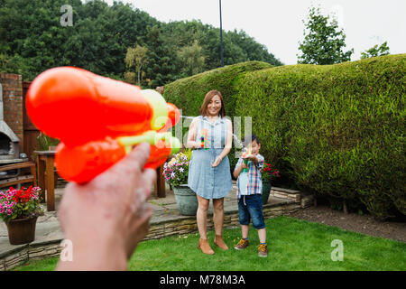 Point de vue d'un homme ayant une lutte de l'eau avec les pistolets à eau dans le jardin avec sa femme et son fils. Banque D'Images