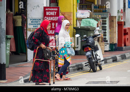 Deux jeunes femmes, et une femme âgée à l'aide d'un dispositif d'aide à la marche, traversant la rue à Singapour. Banque D'Images