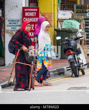 Deux jeunes femmes, et une femme âgée à l'aide d'un dispositif d'aide à la marche, traversant la rue à Singapour. Banque D'Images