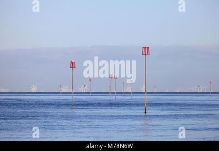 Épi rouge marqueurs sur la côte de Norfolk à Heacham avec une ferme éolienne en mer du Nord dans l'arrière-plan. Banque D'Images