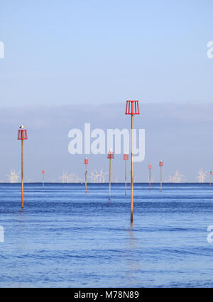 Épi rouge marqueurs sur la côte de Norfolk à Heacham avec une ferme éolienne en mer du Nord dans l'arrière-plan. Banque D'Images