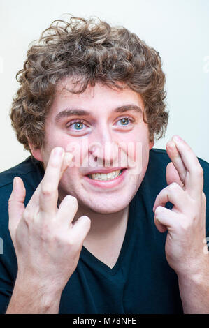 Portrait of young man holding curly aventureuse drôle les doigts croisés dans l'espoir sur fond blanc. Banque D'Images