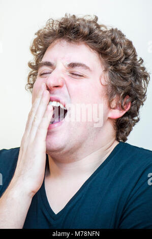 Portrait of young Caucasian ethnicité fatigué le bâillement curly homme couvre sa bouche ouverte sur fond blanc. Banque D'Images
