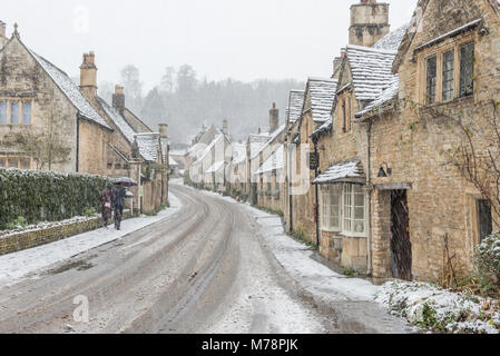 Un couple en train de marcher jusqu'à la colline à Castle Combe avec un parapluie en les protégeant des fortes chutes de neige, Wiltshire, Angleterre, Royaume-Uni, Europe Banque D'Images