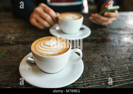 Deux tasses de café sur une table en bois, un homme tenant une dans sa main et vont à l'appel. En attente d'une réunion. Une autre personne est en retard pour la réunion. Banque D'Images