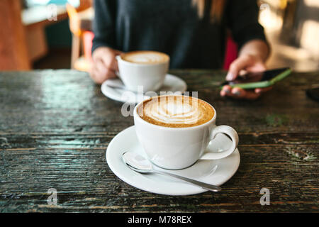 Deux tasses de café sur une table en bois, une jeune fille tenant une dans sa main et vont à l'appel. En attente d'une réunion. Une autre personne est en retard pour la réunion. Banque D'Images