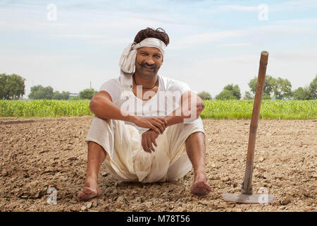 Farmer est assis sur le terrain avec le hoe Banque D'Images