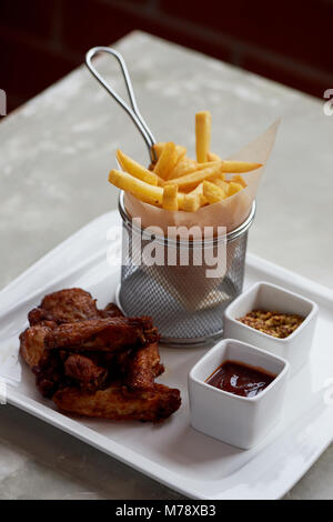 Des ailes de poulet avec sauce ketchup et frites dans un support métallique sur le papier parchemin Banque D'Images