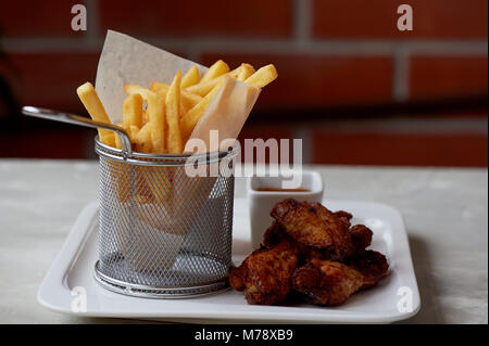 Des ailes de poulet avec sauce ketchup et frites dans un support métallique sur le papier parchemin Banque D'Images