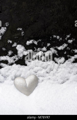 Peint en gris argent coeur placé contre l'ardoise de toiture sur laquelle la neige a réglé. Un paysage en minature imitant la neige qui tombe à travers un ciel sombre Banque D'Images