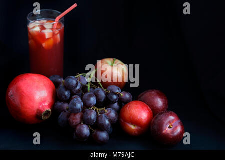 Alimentation - clair-obscur sombre pomegranite, raisins, pommes et prunes avec punch aux fruits sur fond foncé with copy space Banque D'Images