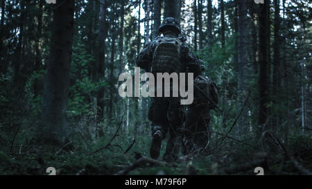 Le Groupe de soldat entièrement équipée se déplace plus loin dans la forêt dense. Elles sont déployées sur la Mission militaire de reconnaissance dans la nuit dans une ambiance sombre. Banque D'Images