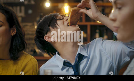 Au bar/ restaurant asiatique faim homme mange Tranche de délicieuses pizzas. Il est entouré d'amis et collègues et a de bons temps. Banque D'Images