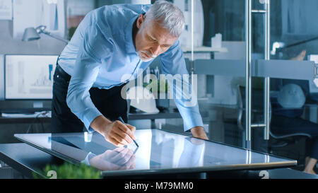 Ingénieur Architecture Senior Concept bâtiment attire sur une tablette graphique Afficher Écran tactile Vertical table. Nettoyer le bureau minimaliste, mur de béton Banque D'Images