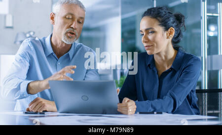 Hommes et femmes d'expérience des employés de bureau discuter Projet en cours tout en travaillant sur un ordinateur portable. Banque D'Images