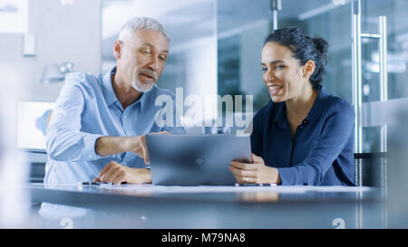 Hommes et femmes d'expérience des employés de bureau discuter Projet en cours tout en travaillant sur un ordinateur portable. Banque D'Images