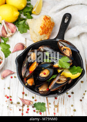 Moules au vin blanc délicieux avec du citron, l'ail, les herbes et les épices dans une poêle en fonte . Baguette, la coriandre et le poivre. Les fruits de mer. Les palourdes dans le elle Banque D'Images