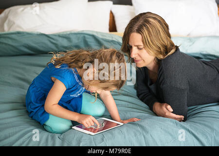 Une femme en regardant sa fille apprendre à écrire à l'aide d'un ipad mini. Banque D'Images