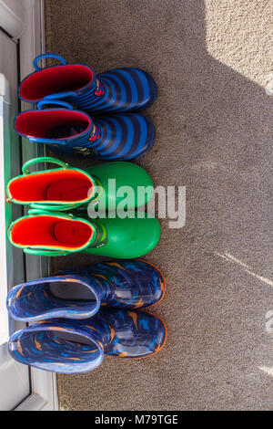 Les jeunes colorés pour enfants wellies assis sur un mat par la porte arrière Banque D'Images