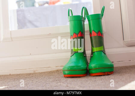 Les jeunes colorés pour enfants wellies assis sur un mat par la porte arrière Banque D'Images