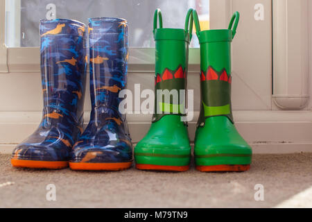 Les jeunes colorés pour enfants wellies assis sur un mat par la porte arrière Banque D'Images