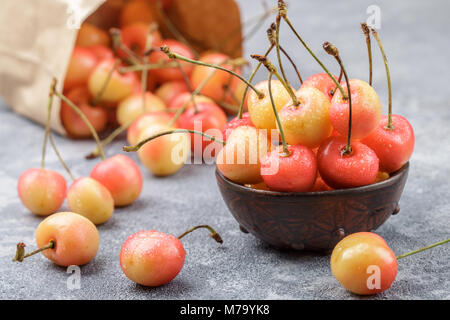 Cerises Rainier rouge et jaune avec des gouttes d'eau dans une cuvette d'argile sur la surface de béton gris. Selective focus Banque D'Images