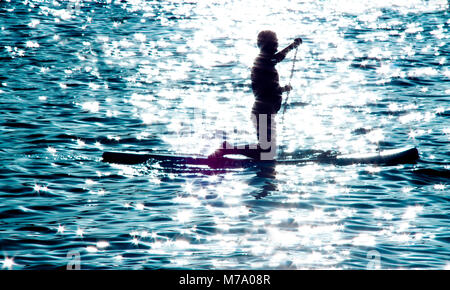 Silhouette floue d'un homme à genoux on paddle board et de l'aviron dans le clair de lune sur la mer, l'eau fait allumé sport loisirs pour l'esprit et le corps Banque D'Images