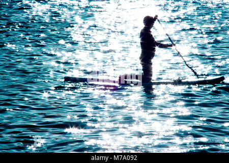 Silhouette floue d'un homme à genoux on paddle board et de l'aviron dans le clair de lune sur la mer, l'eau fait allumé sport loisirs pour l'esprit et le corps Banque D'Images