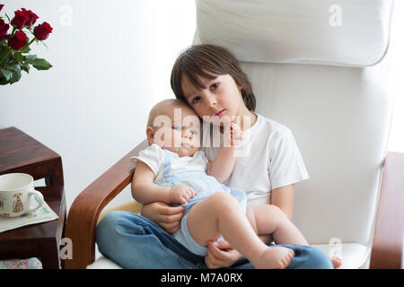 Adorable enfant d'âge préscolaire, serrant son petit frère dans un rocking-chair, smiling at each other Banque D'Images