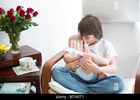 Adorable enfant d'âge préscolaire, serrant son petit frère dans un rocking-chair, smiling at each other Banque D'Images