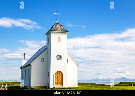 Flateyjarkirkja luthérienne blanche avec prairie en premier plan et la mer fjord avec ciel bleu et les montagnes en arrière-plan, Flatey, Islande Banque D'Images