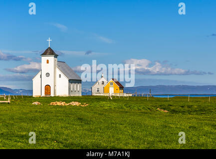 Flateyjarkirkja luthérienne blanche et de couple de la vie abris avec prairie en premier plan et la mer fjord avec ciel bleu en arrière-plan, Flatey, Icel Banque D'Images