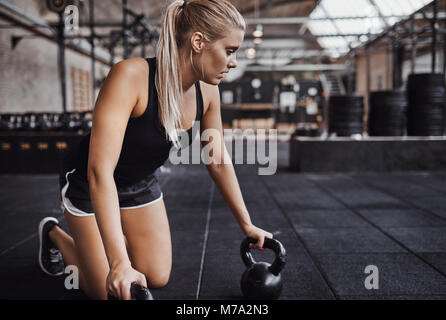 Fit young blonde woman in sportswear à genoux sur un plancher du gymnase de la préparation à l'exercice avec des poids Banque D'Images
