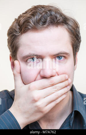 Calme, garder le silence. Portrait of young blue-eyed man holding sa bouche fermée avec doigts sur fond blanc. Banque D'Images