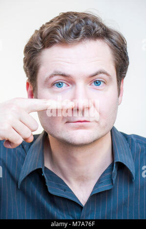 Portrait of young Caucasian ethnicité blue-eyed man points sur son nez sur fond blanc. Pièces à visage humain. Banque D'Images