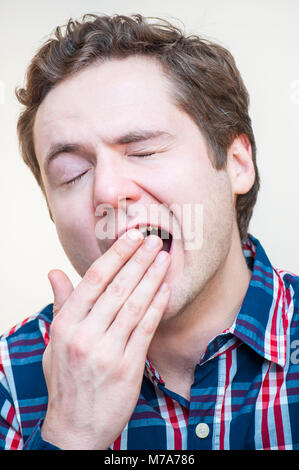 Portrait de jeune homme bouclé bâillement fatigué couvre sa bouche ouverte avec palm sur fond blanc. Banque D'Images