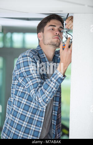 Male electrician fixing la lumière sur le plafond à l'aide d'un tournevis Banque D'Images