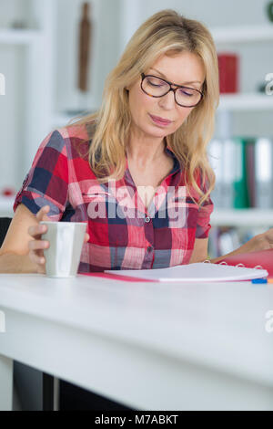 Happy woman sitting with documents financiers dans la cuisine et smiling Banque D'Images