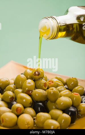 On verse de l'huile d'olive et olives vertes sur fond noir Banque D'Images