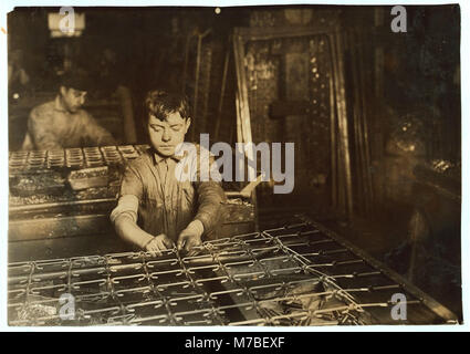 Cette photographie montre deux garçons, âgés de 14 et 15 ans, reliant des ressorts de lit, probablement dans une usine ou un atelier, capturant un moment du travail industriel au début du XXe siècle. Banque D'Images