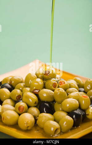 On verse de l'huile d'olive et olives vertes sur fond noir Banque D'Images